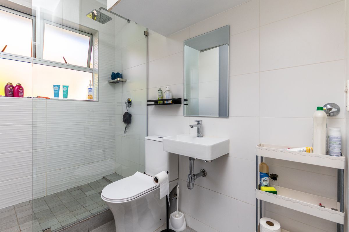 A compact, modern bathroom featuring a glass-enclosed walk-in shower, wall-mounted basin, and toilet with clean white tiling throughout.
