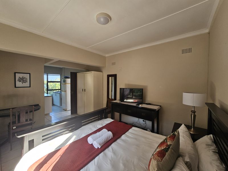 A bedroom featuring tiled flooring, a built-in wardrobe, and coved ceilings, with an open-plan layout connecting to a small kitchen area.
