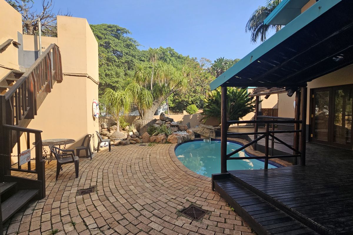 Outdoor pool area featuring a swimming pool, timber decking, a pergola, and brick paving, set within a landscaped garden environment.