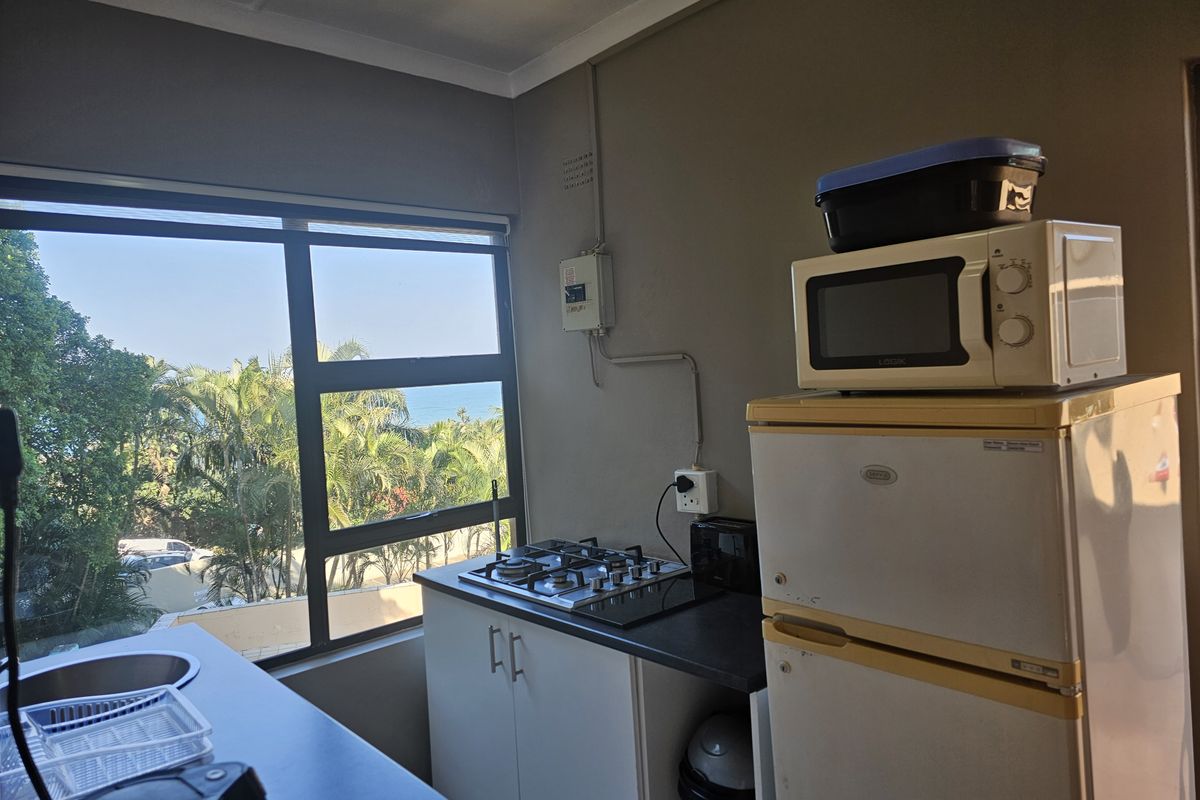 Compact kitchen area featuring a gas hob, built-in cabinetry, and a large window with scenic coastal views.