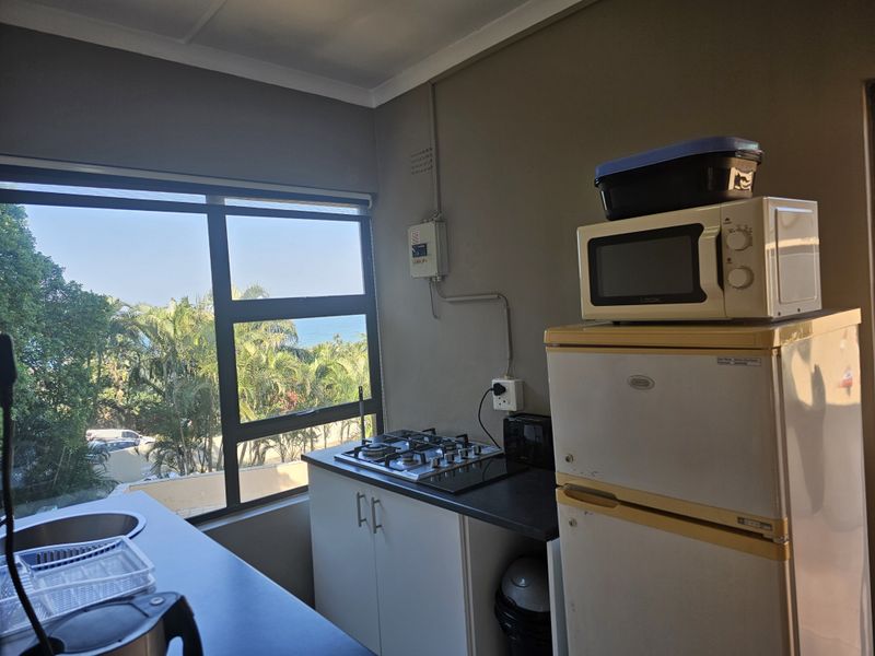 Compact kitchen area featuring a gas hob, built-in cabinetry, and a large window with scenic coastal views.