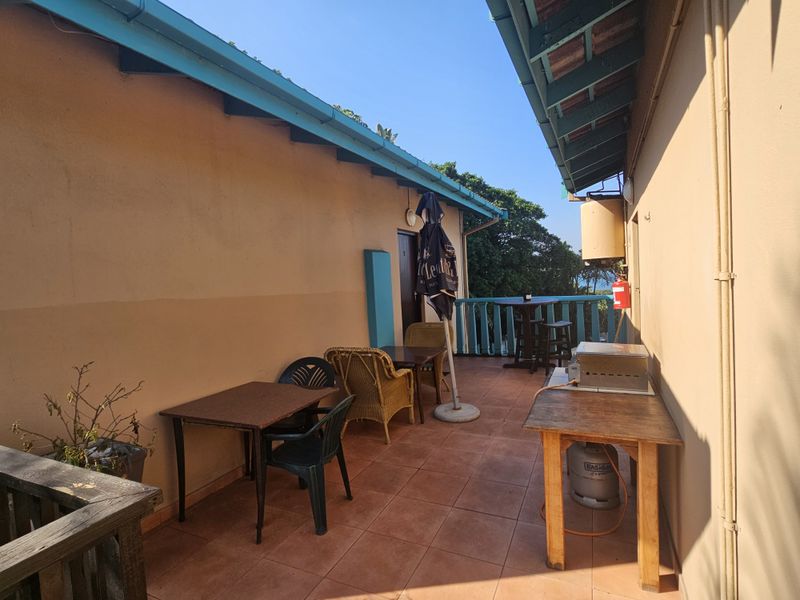 Spacious outdoor balcony area featuring tiled flooring, a protective balustrade, and exposed roof rafters, offering a functional space for outdoor relaxation.