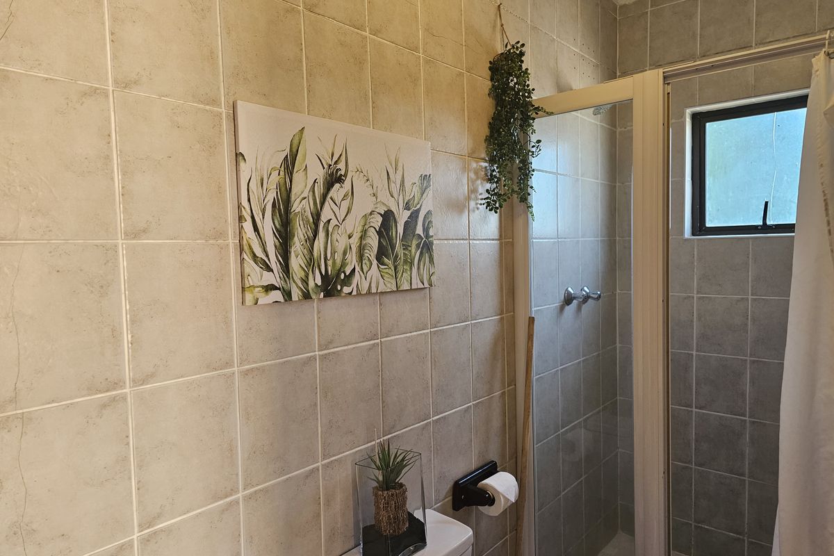 A functional bathroom featuring full-height ceramic wall tiling, a shower enclosure, and a standard toilet suite.