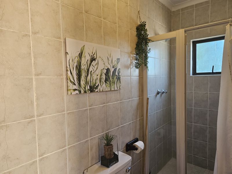 A functional bathroom featuring full-height ceramic wall tiling, a shower enclosure, and a standard toilet suite.