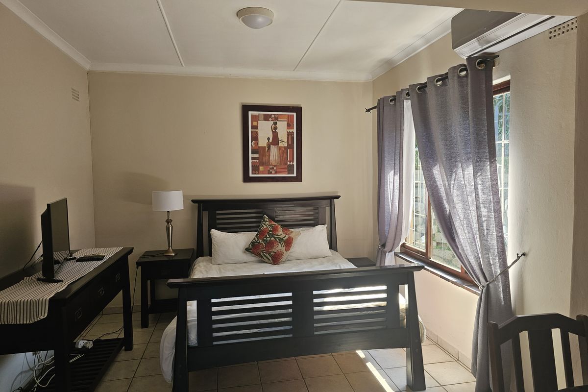 A well-lit bedroom featuring tiled flooring, an integrated air conditioning unit, and a window fitted with security bars.