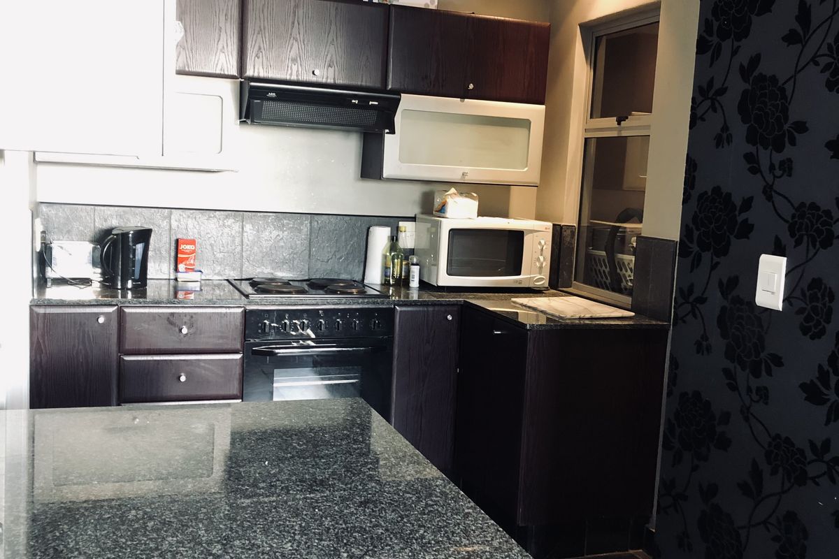 A compact kitchen featuring dark wood cabinetry, granite countertops, a built-in oven with extractor fan, and a breakfast island.