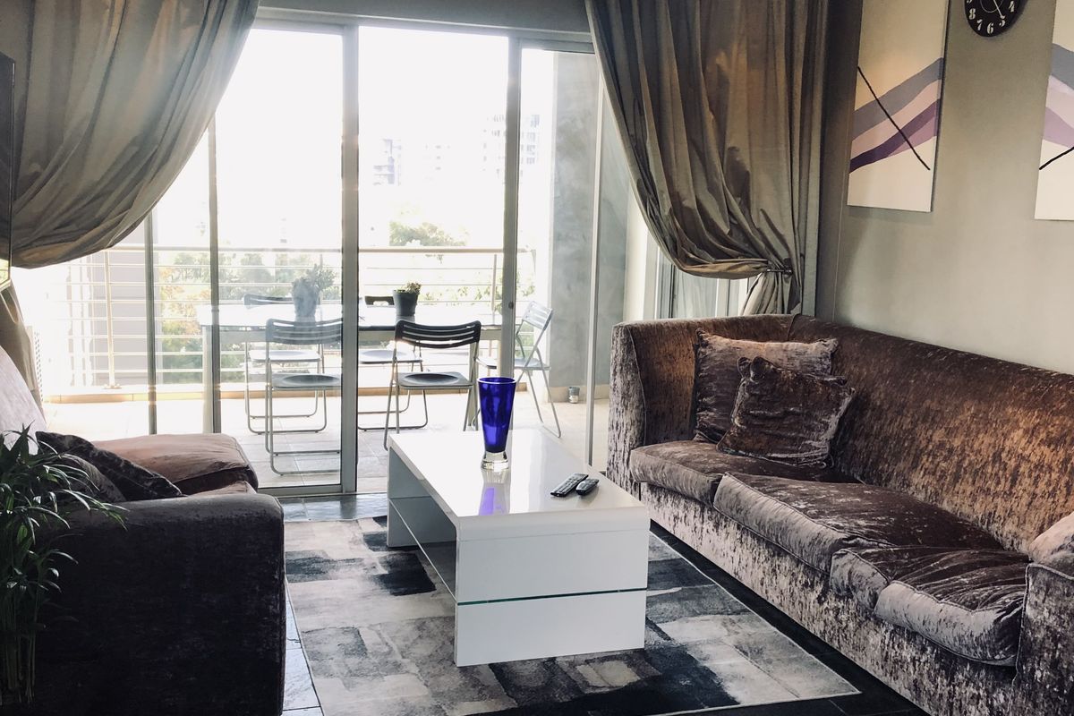 A comfortable living room featuring dark tiled flooring and large sliding glass doors that open onto a private balcony, providing ample natural light.