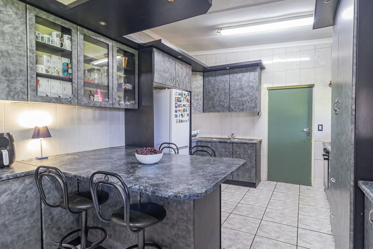 A functional kitchen featuring grey laminate cabinetry, tiled backsplash, and a breakfast bar area with tiled flooring.