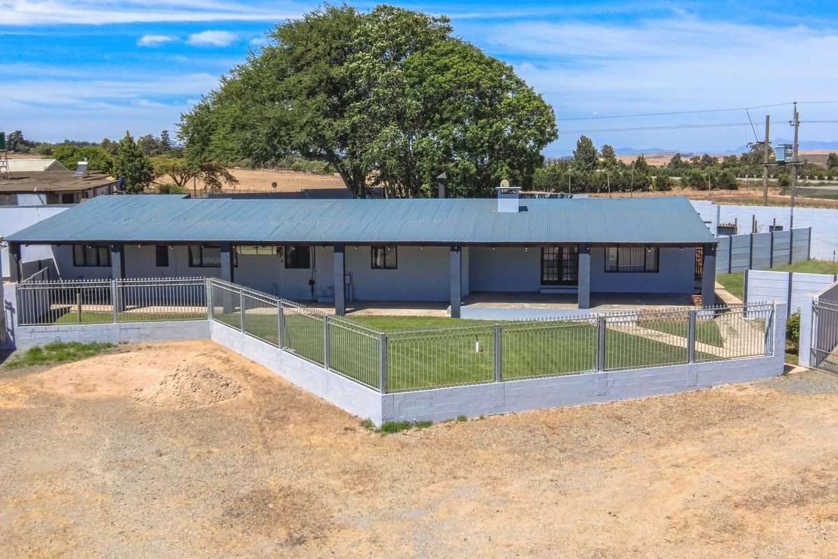 Rear view of a farm property featuring a covered patio, corrugated metal roof, and secure perimeter fencing enclosing a lawn area.