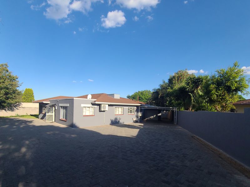 Front exterior view of the house featuring a large paved driveway, perimeter wall, and a covered carport area.