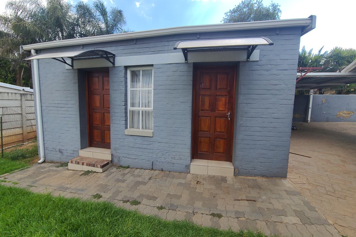 Exterior view of a painted brick outbuilding featuring two timber doors, window, and a paved patio area.