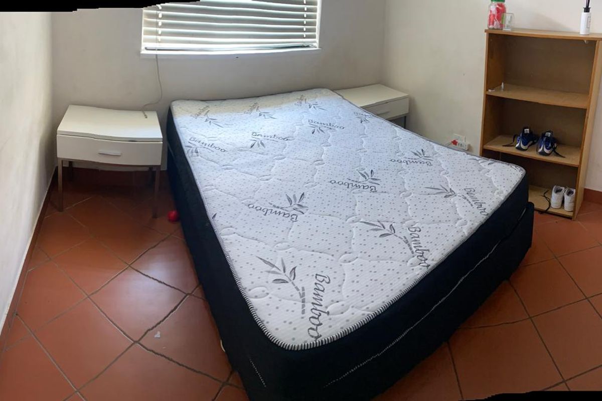 A bedroom featuring tiled flooring and venetian blinds, currently showing signs of wear including cracked floor tiles.