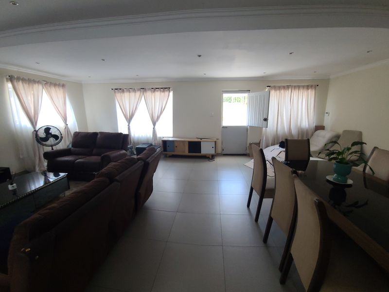 Spacious open-plan living and dining area featuring neutral tiled flooring, recessed downlighting, and decorative ceiling cornicing.