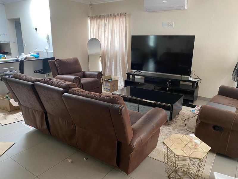 A functional living room featuring tiled flooring and a wall-mounted split-system air conditioner, with an open-plan layout connecting to the kitchen area.