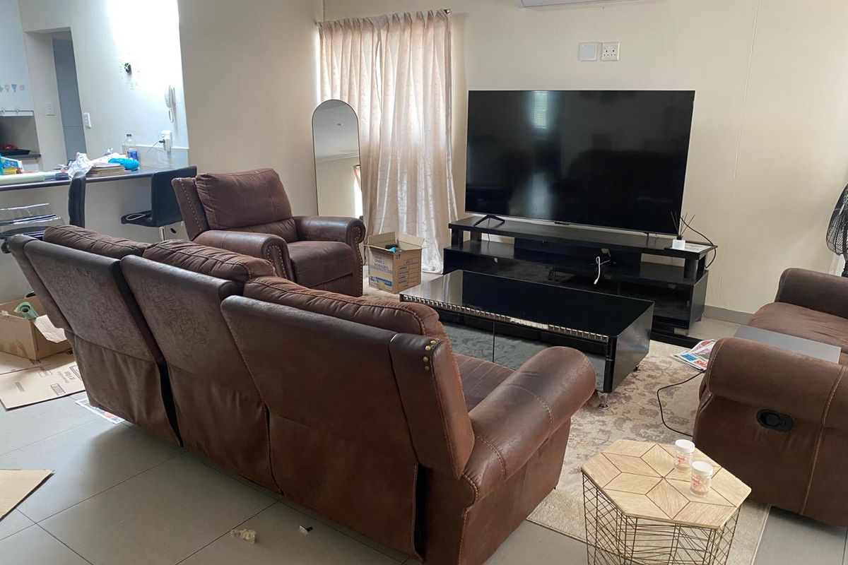 A functional living room featuring tiled flooring and a wall-mounted split-system air conditioner, with an open-plan layout connecting to the kitchen area.