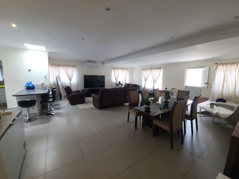 Spacious open-plan living and dining area featuring tiled flooring, recessed lighting, a breakfast bar, and a skylight, creating a bright and functional layout.