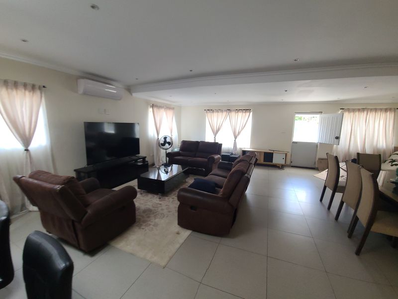Spacious open-plan living and dining area featuring neutral tiled flooring, recessed lighting, and a wall-mounted air conditioning unit.