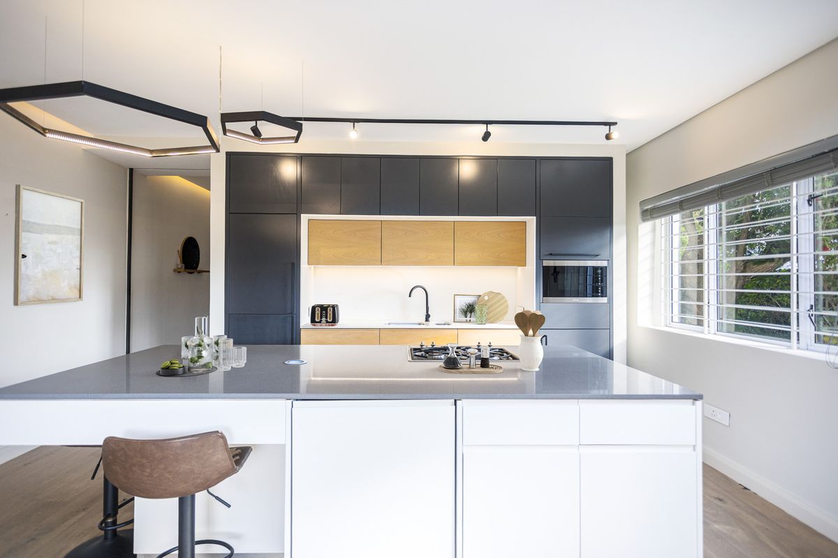 Modern kitchen featuring a large central island with a built-in gas hob, sleek two-tone cabinetry, integrated appliances, and contemporary track lighting.