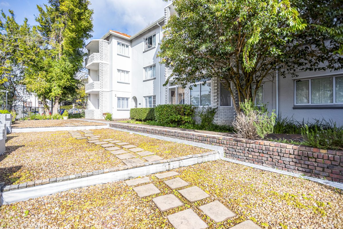 Exterior view of the apartment building featuring a landscaped garden area with brick retaining walls and paved stepping stones.