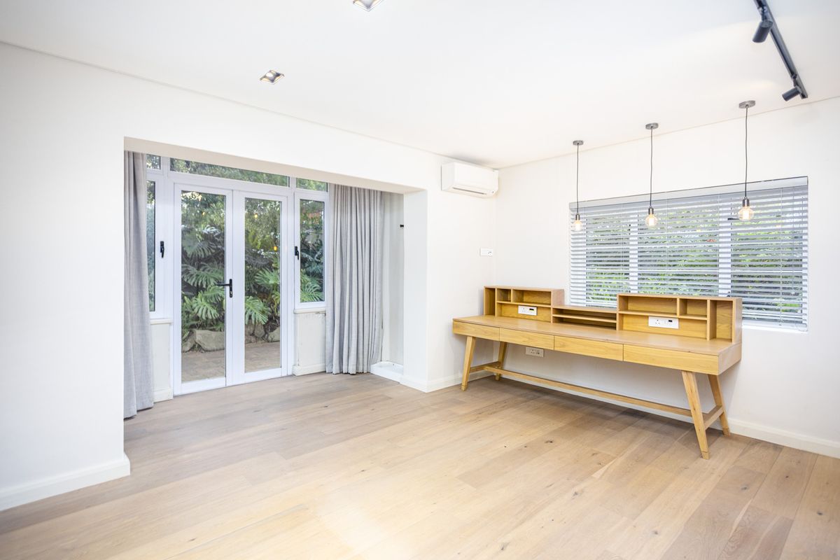 Bright living area featuring light wood flooring, recessed lighting, a wall-mounted air conditioning unit, and double glass doors leading to a private garden.