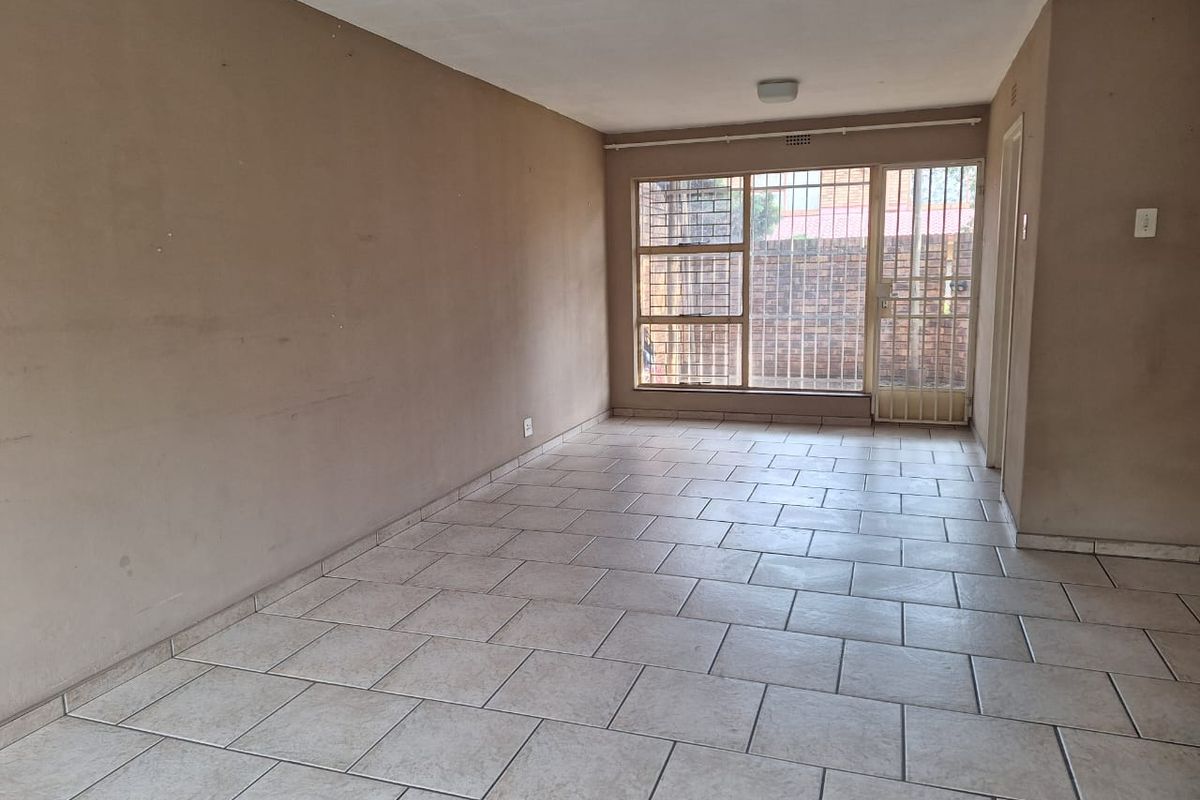 An empty living room featuring neutral tiled flooring, large windows with security bars, and a security gate leading to the exterior.