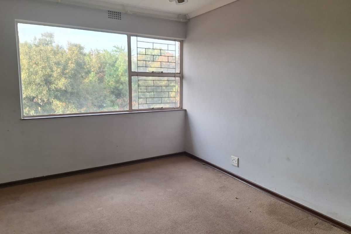 An empty bedroom featuring a large window with security bars, carpeted flooring, and a ceiling fan.