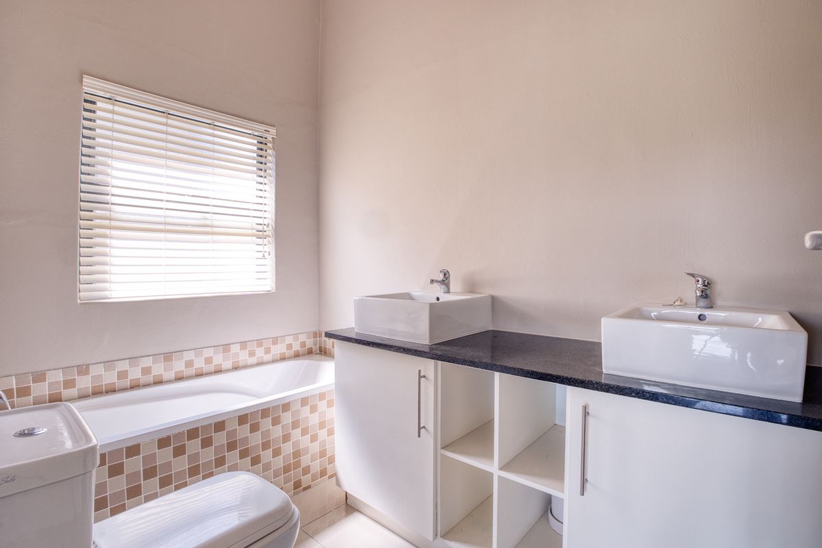 A modern bathroom featuring a dual vanity with vessel sinks, a built-in bathtub with tiled surround, and a window with fitted blinds.