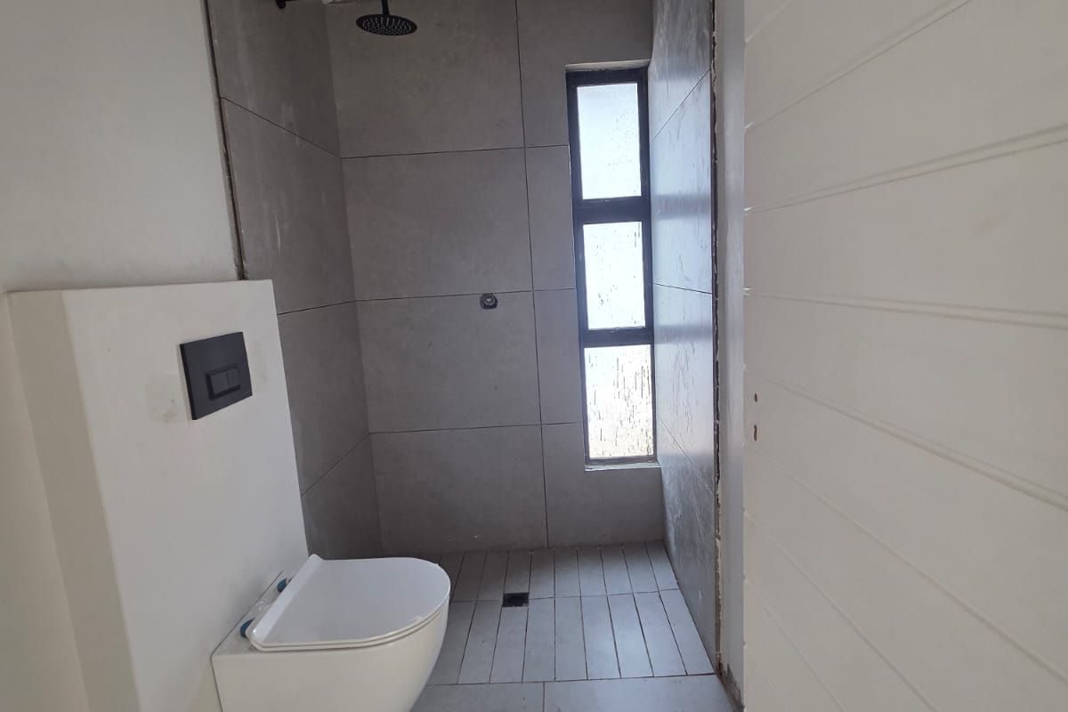 A modern, minimalist bathroom featuring a wall-mounted toilet with a concealed cistern and a walk-in shower area with grey tiling.