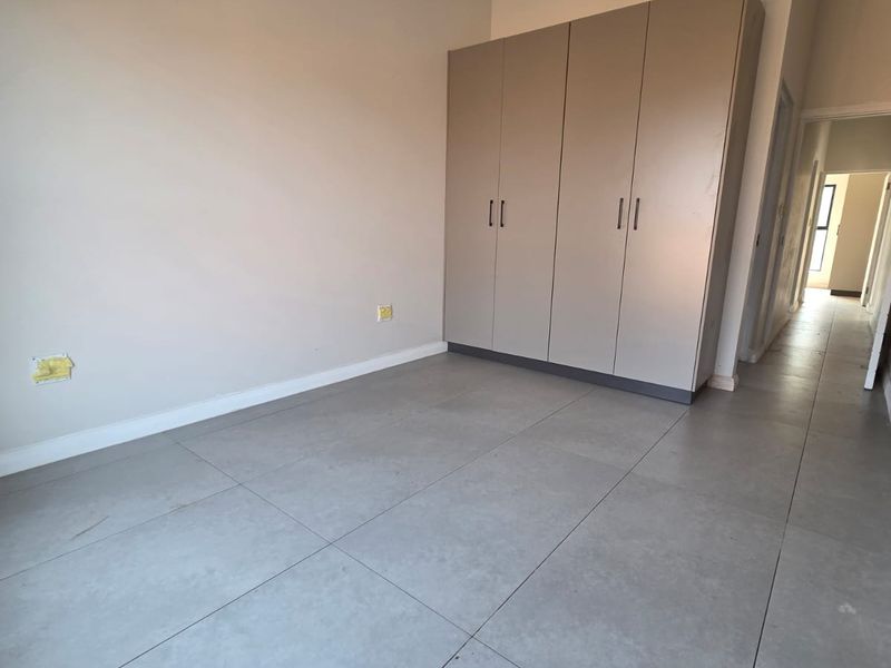 A bright, empty bedroom featuring neutral walls, large format floor tiles, and a modern built-in wardrobe with clean lines.