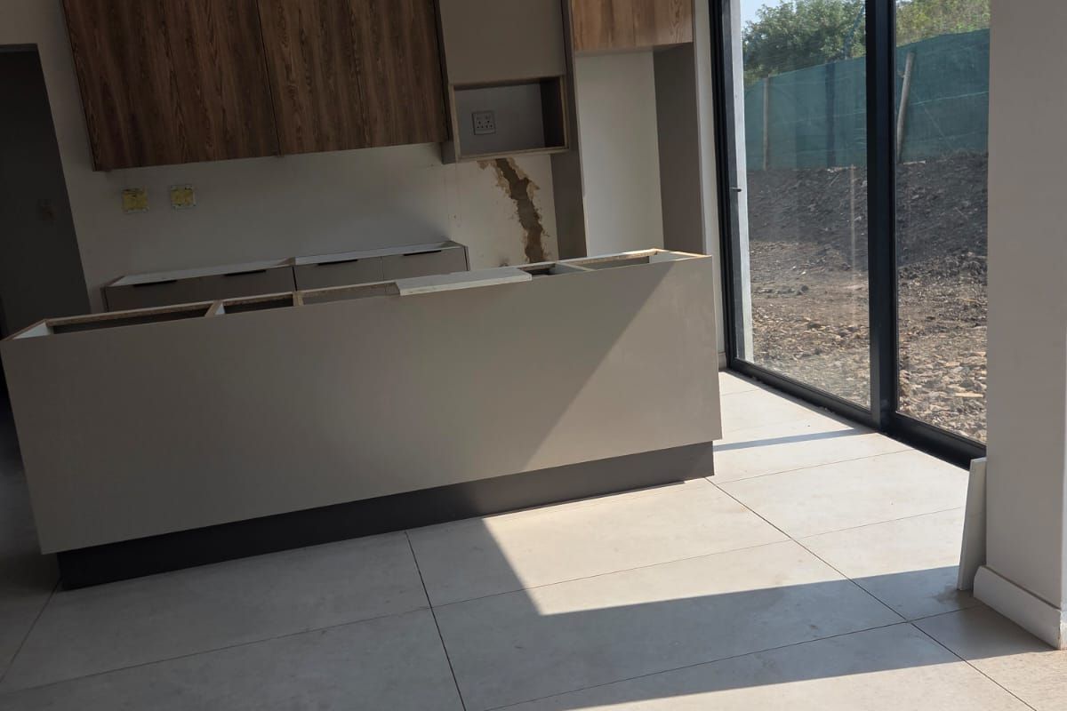 An unfinished kitchen space featuring modern cabinetry, a central island, and large format floor tiles, with direct access to the exterior via sliding glass doors.