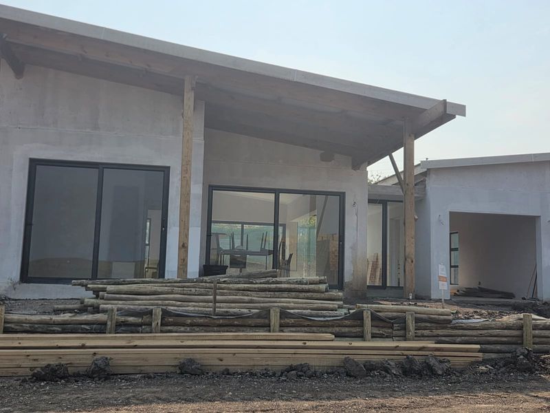 Rear view of a house under construction featuring large sliding glass doors, timber support beams, and an unfinished concrete facade.