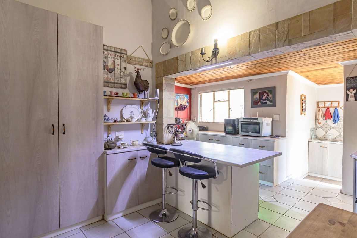A functional kitchen featuring a central breakfast bar, built-in cabinetry, tiled flooring, and a timber-paneled ceiling section.