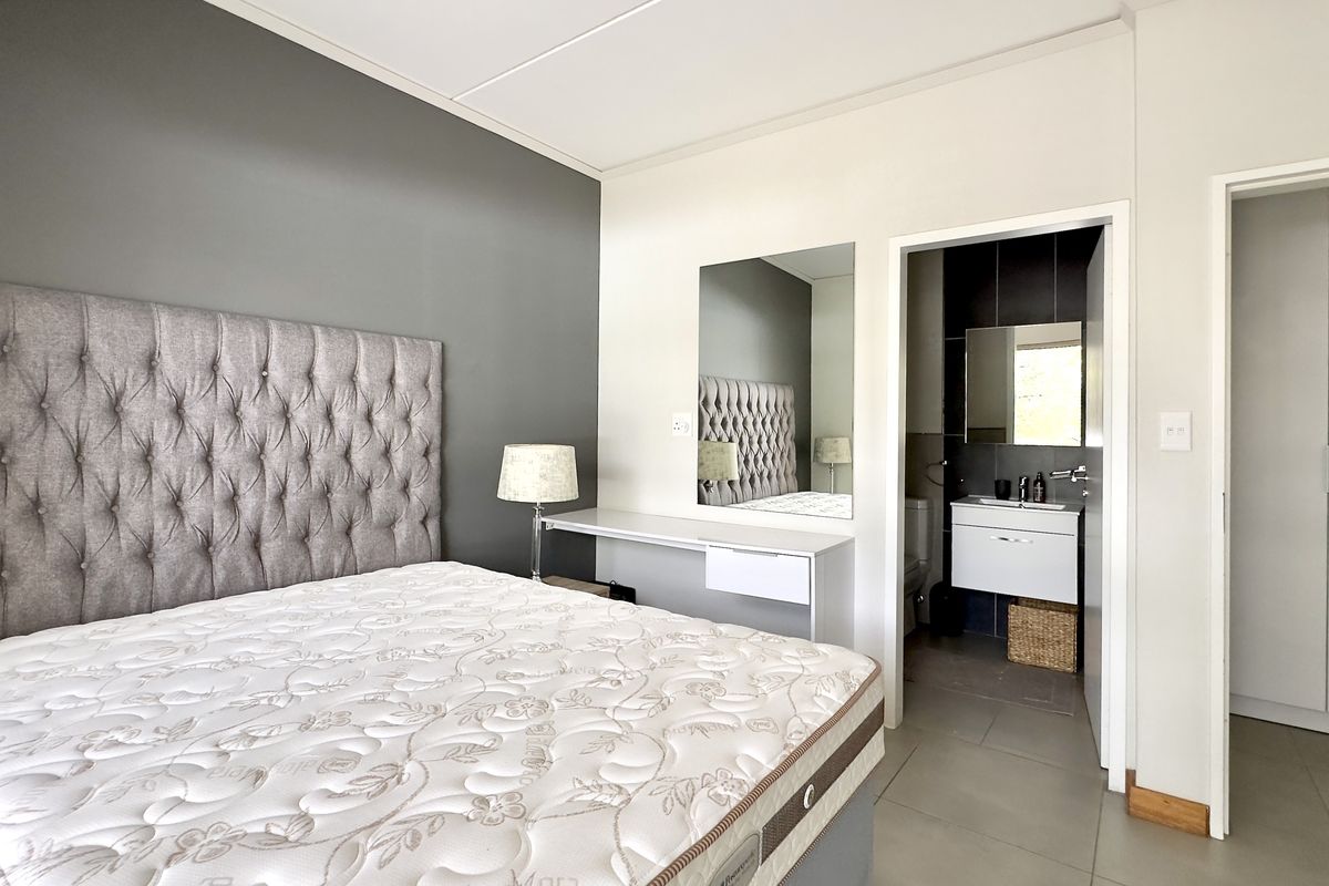 A well-maintained bedroom featuring a built-in vanity, integrated mirror, and an en-suite bathroom with modern fixtures and tiled flooring.