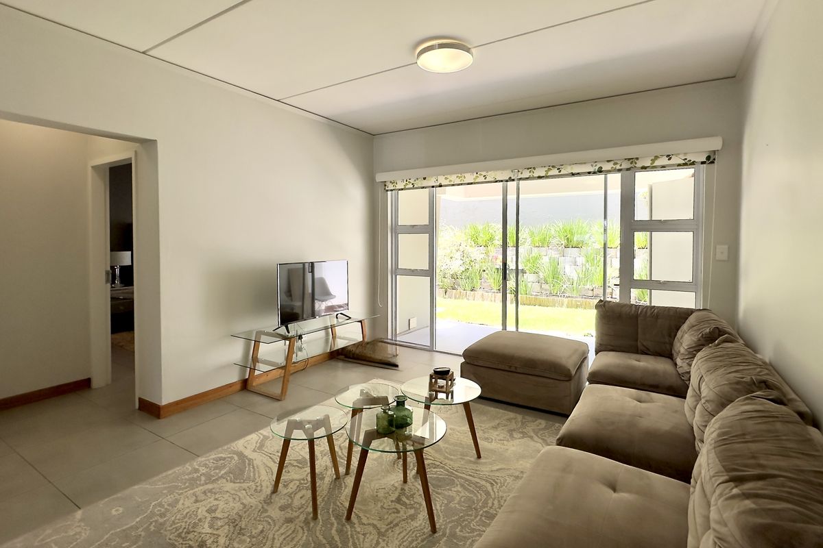 A bright living room featuring large sliding glass doors that open onto a private patio and garden area, with neutral tiled flooring throughout.