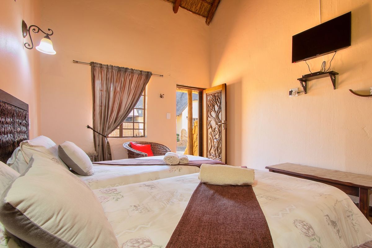 A cozy bedroom featuring a high thatched ceiling with exposed timber rafters, a decorative carved wooden door, and warm ambient lighting.