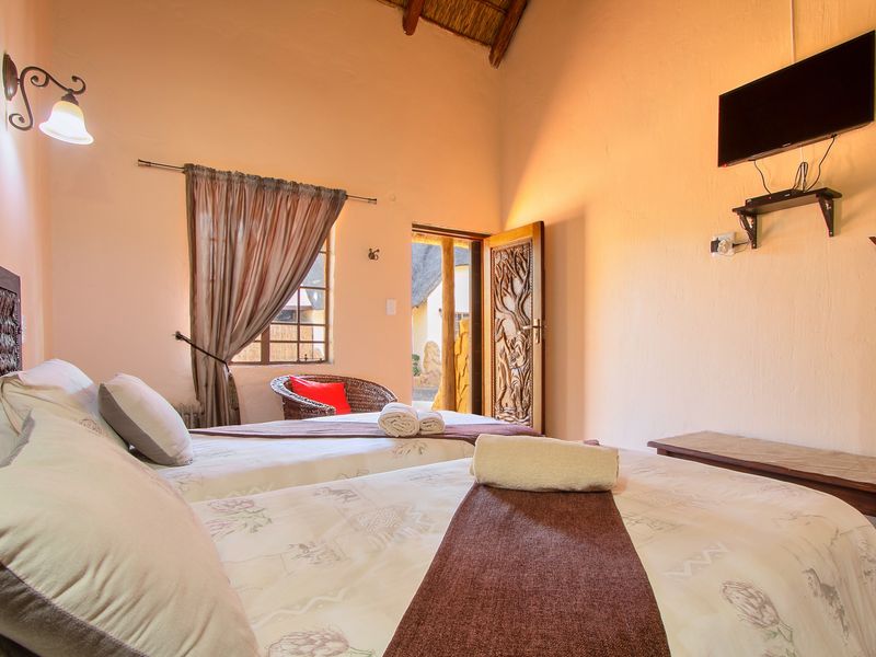 A cozy bedroom featuring a high thatched ceiling with exposed timber rafters, a decorative carved wooden door, and warm ambient lighting.
