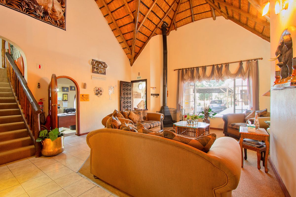Spacious lodge living area featuring a high vaulted thatched ceiling with exposed rafters, a central fireplace, and a staircase leading to the upper level.