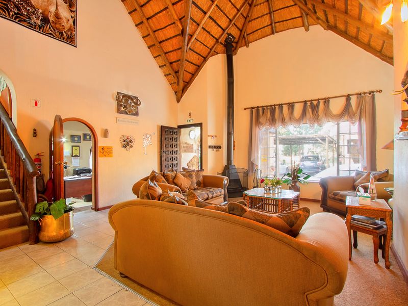 Spacious lodge living area featuring a high vaulted thatched ceiling with exposed rafters, a central fireplace, and a staircase leading to the upper level.