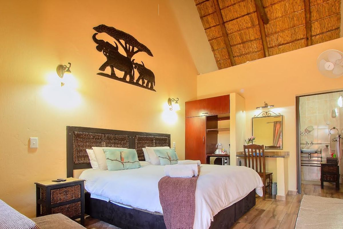 A cozy bedroom featuring a traditional thatched roof with exposed rafters, tiled flooring, and an integrated wardrobe, offering direct access to an en-suite bathroom.