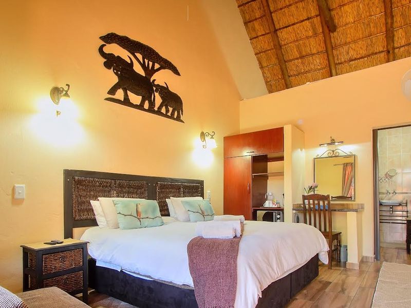 A cozy bedroom featuring a traditional thatched roof with exposed rafters, tiled flooring, and an integrated wardrobe, offering direct access to an en-suite bathroom.
