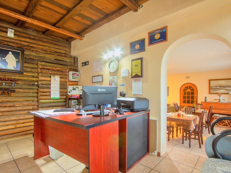 Reception area featuring rustic log wall cladding, exposed timber ceiling beams, and an arched entryway leading into the dining space.