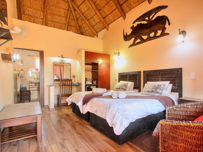 A comfortable bedroom featuring a traditional thatched roof with exposed rafters, tiled flooring, built-in vanity, and an adjoining en-suite bathroom.