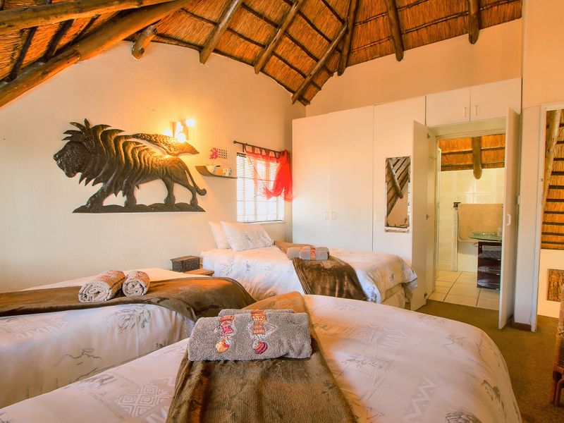 A bedroom featuring a traditional thatched roof with exposed timber rafters, built-in cupboards, and an adjoining en-suite bathroom.