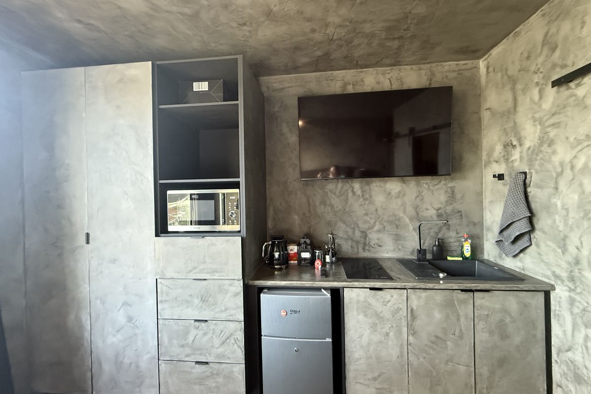 Compact modern kitchenette featuring concrete-effect cabinetry, integrated microwave, induction hob, and a sleek black sink with matching tapware.