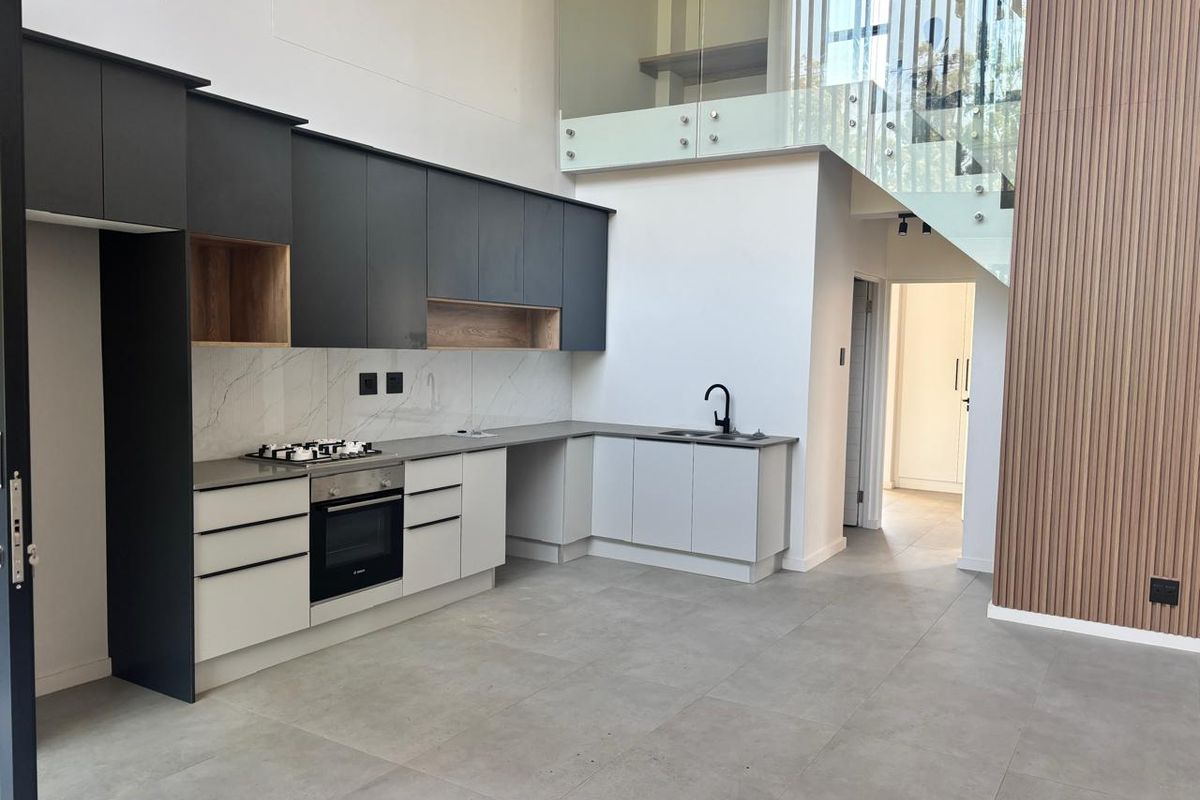 Modern open-plan kitchen featuring two-tone cabinetry, stone countertops, integrated appliances, and a striking glass staircase with timber slat feature wall.