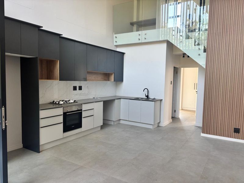 Modern open-plan kitchen featuring two-tone cabinetry, stone countertops, integrated appliances, and a striking glass staircase with timber slat feature wall.