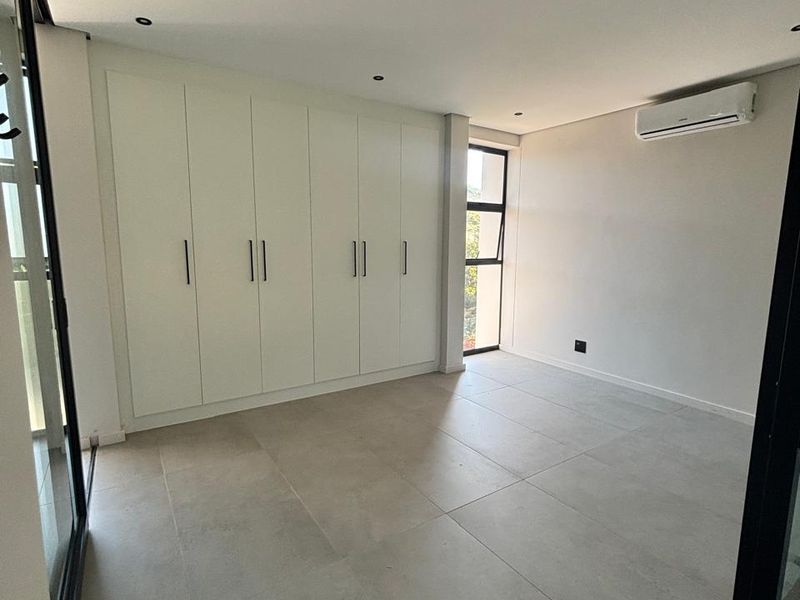 A bright, modern bedroom featuring large-format floor tiles, extensive built-in cabinetry, and a wall-mounted air conditioning unit.