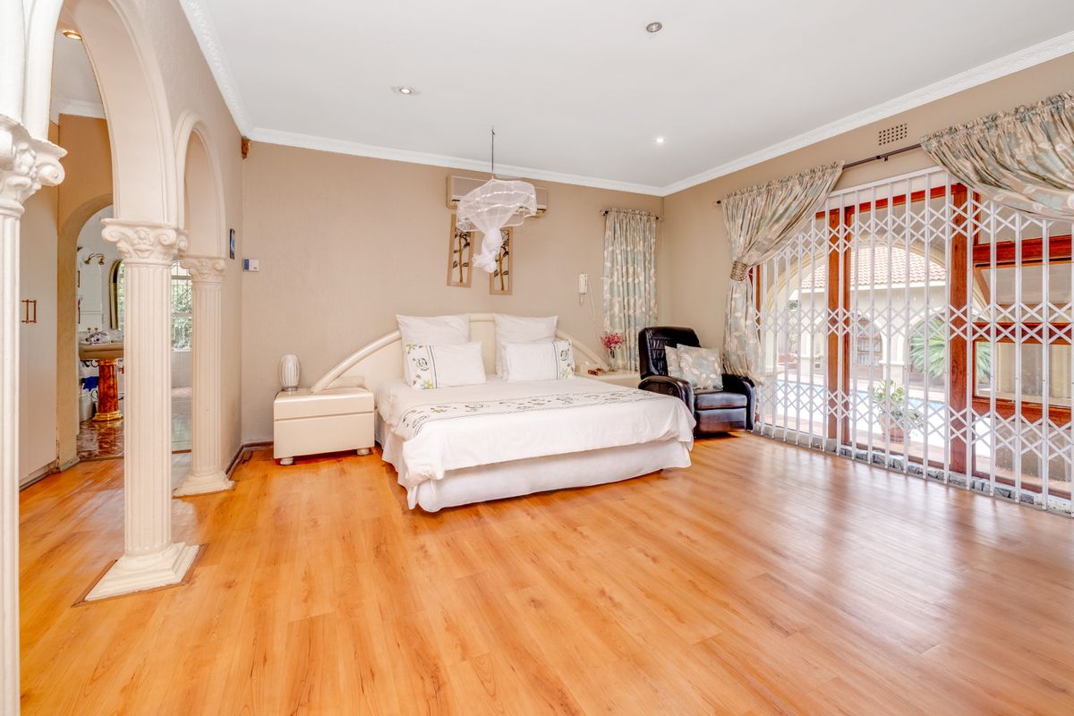 Spacious bedroom featuring laminate flooring, decorative archway entrance, built-in air conditioning unit, and sliding glass doors with security gate leading to the pool area.