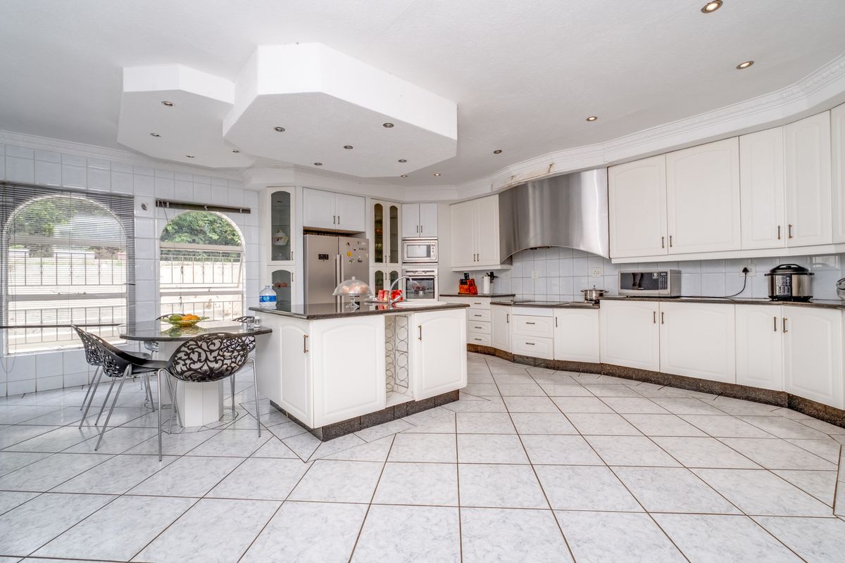 Spacious kitchen featuring white cabinetry, granite countertops, a central island, stainless steel extractor fan, and tiled flooring with integrated dining area.