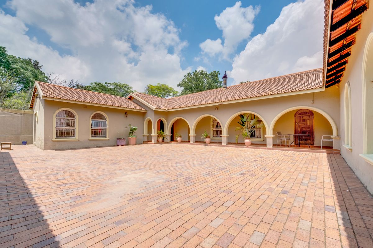 A spacious rear courtyard featuring a paved patio area with covered arched walkways and terracotta roof tiles.